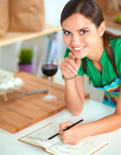 Happy Beautiful Woman Standing In Her Kitchen Writing On A Notebook At