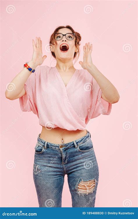 verraste overemotionele meid met een roze bovenlaag en spijkerbroek kijkt op stock foto image