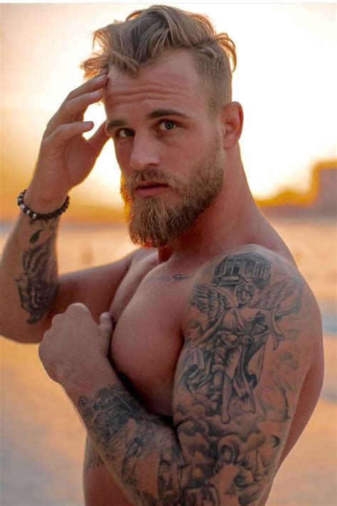 A Man With Tattoos On His Arms And Chest Standing In Front Of The Ocean