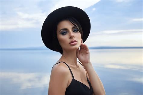 Premium Photo Perfect Brunette Beauty Woman In A Black Hat And A Black Dress Poses Near A Lake