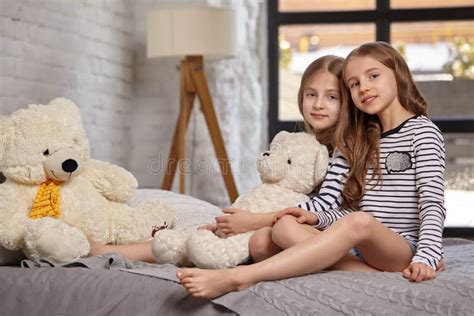 The Image Of Two Little Sisters Sitting On The Bed In The Room Stock