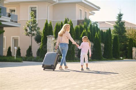Blonde Woman Carrying A Suitcase And Holding Her Daughters Hand Stock