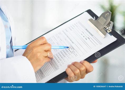 Close Up Of A Female Doctor Filling Up Medical Form At Clipboard While