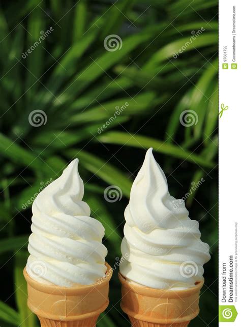 Pair Of Vanilla Soft Serve Ice Cream Cones In The Sunlight With Green Foliage In Background