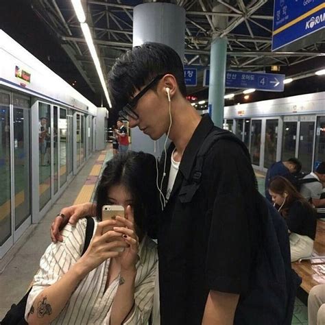 Two People Standing Next To Each Other In Front Of A Train Station