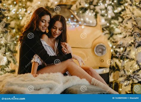 Lesbian Couple Sits Against Background Of Christmas Decorations And