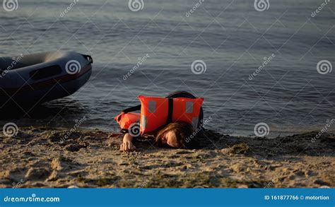 Woman In Life Jacket Lying On Shore Near Boat Victim Of Shipwreck