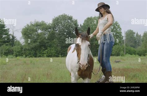 Cowgirl Mounting Her Adult Pinto Horse In A Field Slow Motion Full