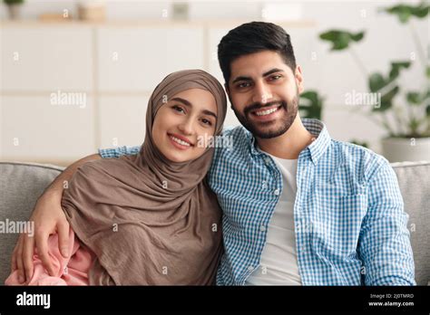 Smiling Middle Eastern Couple Embracing Sitting On Couch At Home Stock