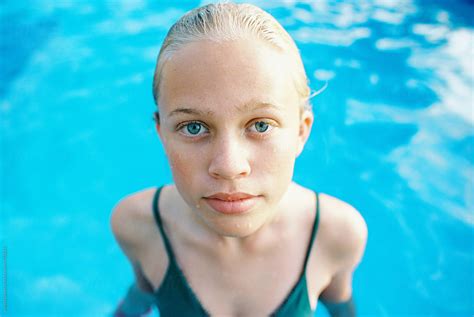blonde teen girl with short hair slicked back in green one piece in swimming pool by stocksy