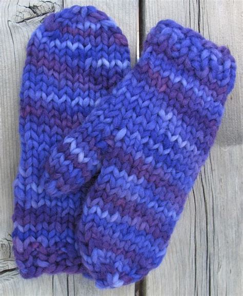 Two Purple Knitted Mittens Hanging On A Wooden Fence