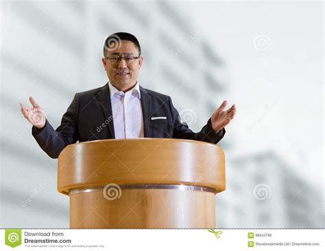 Businessman On Podium Speaking At Conference With Buildings Stock Photo