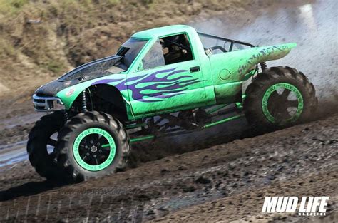A Green Monster Truck With Flames On It S Tires Is Driving Through The Mud