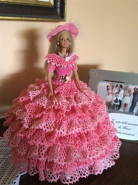 a barbie doll wearing a pink crocheted dress and hat sitting on a table