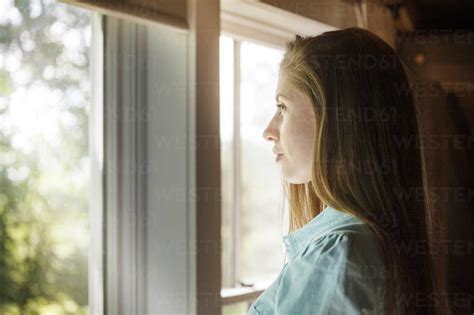 Side View Of Woman Looking Through Window At Home Stock Photo