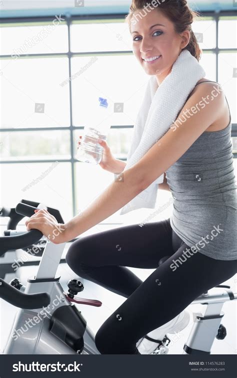 Woman Riding An Exercise Bike And Drinking A Bottle Of
