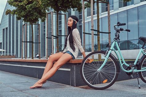 一个穿着上衣和短裤的感嬉皮女的肖像赤脚坐在城市自行车附近的长凳上高清图片下载 正版图片502657465 摄图网