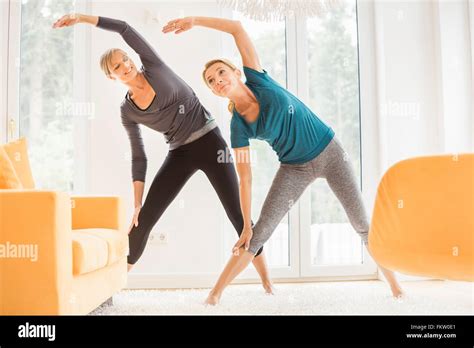 Two Mature Women Bending Over Sideways Whilst Exercising In Living Room