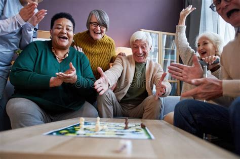 Excited Senior People Playing Board Games At Retirement Home And