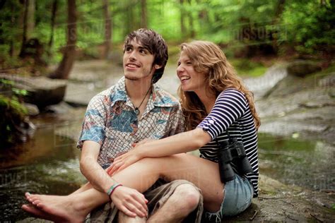 Couple sitting barefoot on boulders in forest - Stock Photo - Dissolve