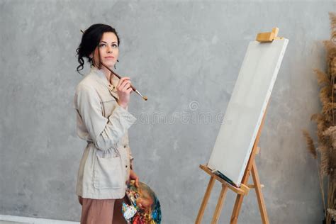 A Female Artist Stands At An Easel With A Brush And Is About To Paint A