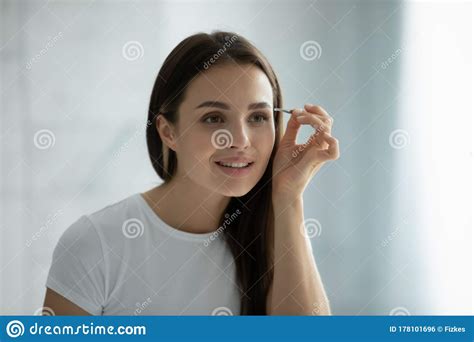 Young Woman Look In Mirror Pinching Eyebrows With Tweezers Stock Photo
