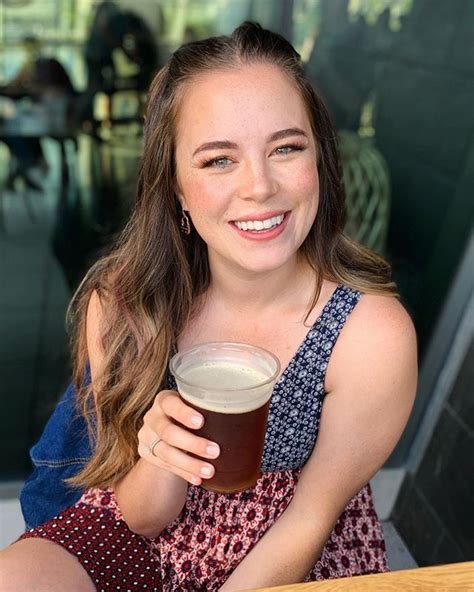 A Woman Sitting At A Table With A Beer In Her Hand And Smiling For The Camera