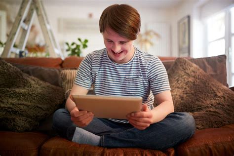 Young Downs Syndrome Man Sitting On Sofa Using Digital Tablet At Home Stock Image Image Of
