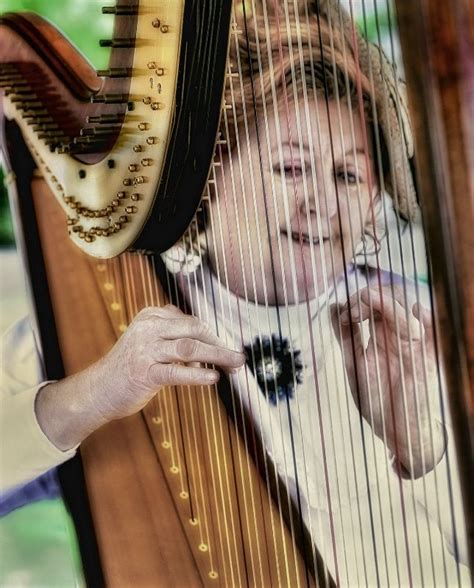 A Woman Holding A Harp And Smiling At The Camera With Her Hand On Its