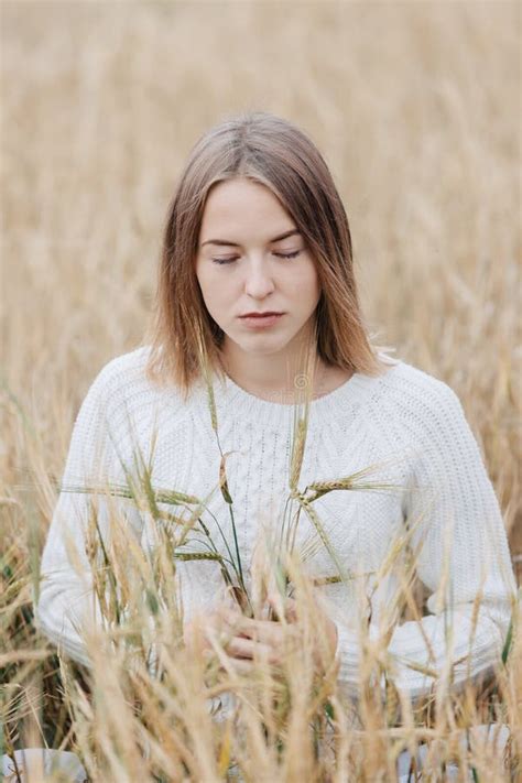 Beautiful Young Girl In A White Sweater Sits In A Wheat Field Stock