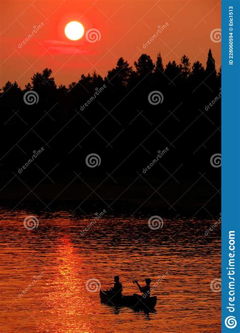 Two People In Canoe Fishing In Lake River At Sunset Or Sunrise