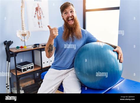rothaariger mann mit langem bart der den pilates ball in der rehabilitationsklinik hält und den