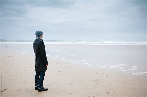 Man Standing Alone On The Beach Looking Out To Sea Stocksy United