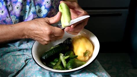 Female Mature Hands Peel And Cut Cucumber Into Bowl Of Fresh Vegetables