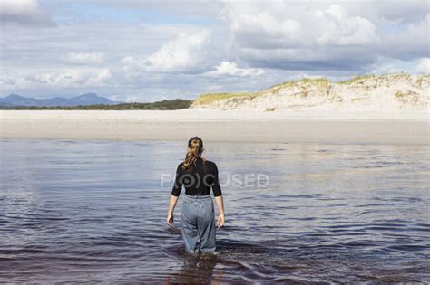 A Teenage Girl Wading Through A Water Channel On A Wide Sandy Beach