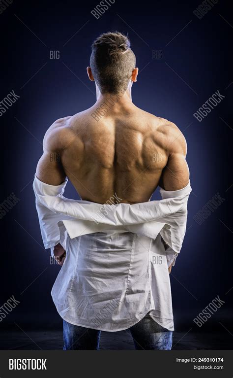 Rearview Of Back Of Male Bodybuilder Opening His Shirt Revealing Muscular Torso On Black