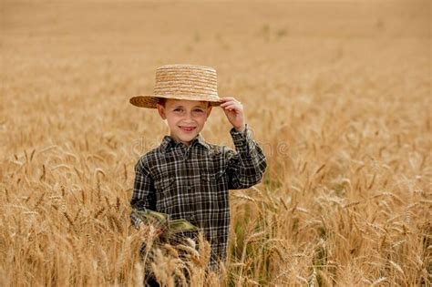 A Smiling Little Farmer Boy In A Plaid Shirt And Straw Hat Poses For A