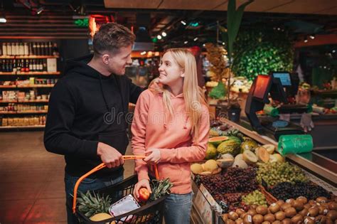 Young Couple In Grocery Store Cheerful Man And Woman Look At Each Other And Smile He Hold