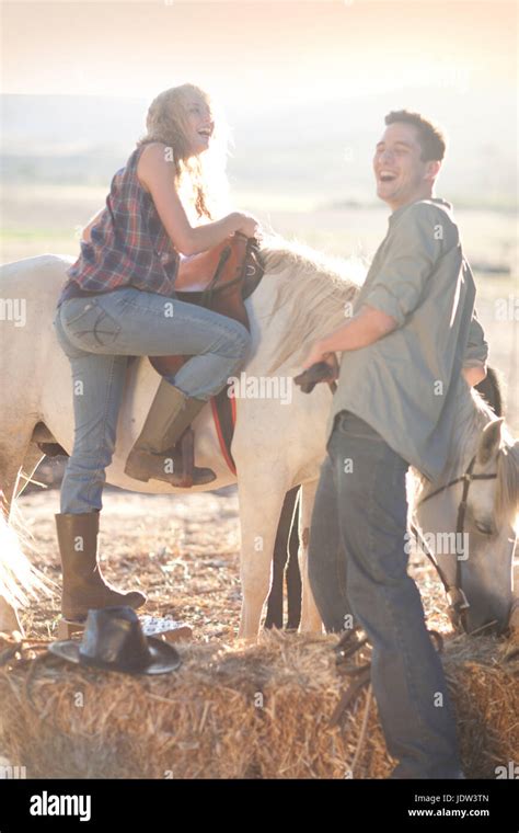 Young Woman Mounting Horse With Man Laughing Stock Photo Alamy