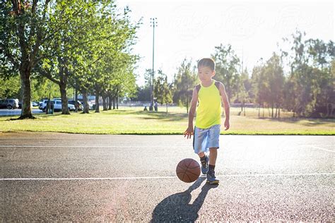 Asian Kid Dribbling A Basketball In An Outdoor Basketball Court By