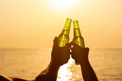 Premium Photo Couple Hands Holding Beer Bottles Clanging At The Beach In Summer Sunset