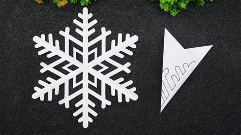 Two Paper Snowflakes Sitting On Top Of A Black Surface Next To Green Plants