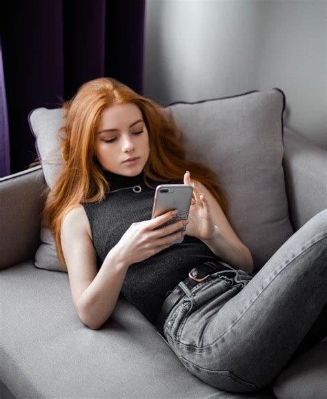 A Woman Sitting On A Couch Looking At Her Cell Phone While She S Using It