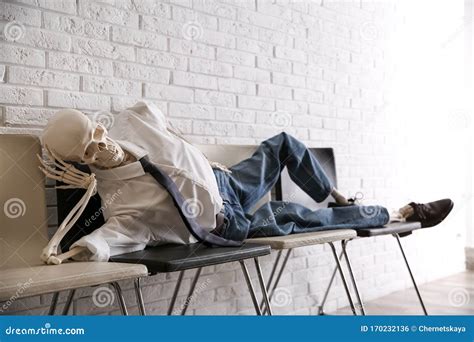 Human Skeleton In Office Wear Lying On Chairs Near Wall Indoors Stock