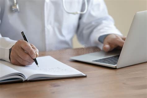 Close Up Of Male Doctor Work On Computer Making Notes Stock Image