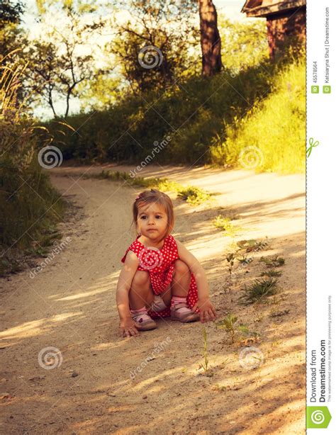 Little Cute Girl In Red Dress Is Sitting On The Road Stock