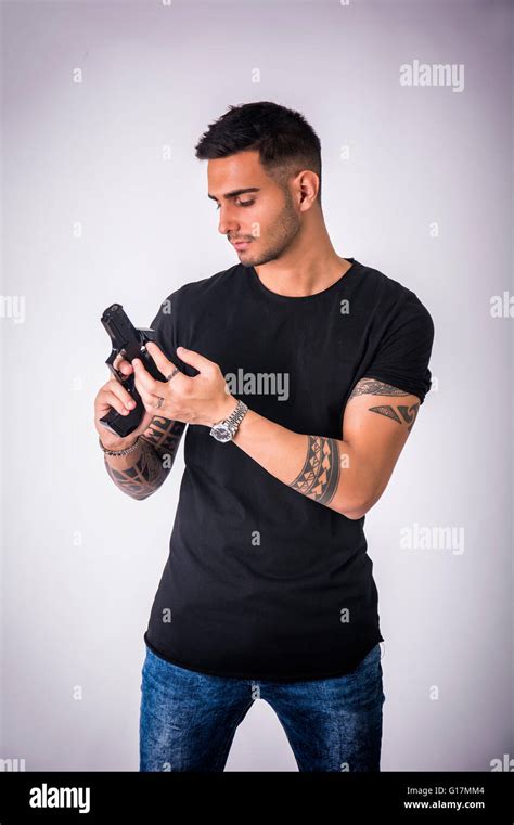 Young Handsome Man Holding A Hand Gun Wearing Black T Shirt On Light