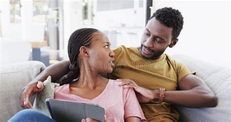 African American Couple Lying On Bed Using Smartphone And Tablet Talking At Home In Slow