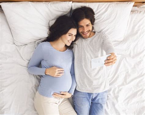 Pregnant Couple Taking Selfie While Lying In Bed Together Stock Image