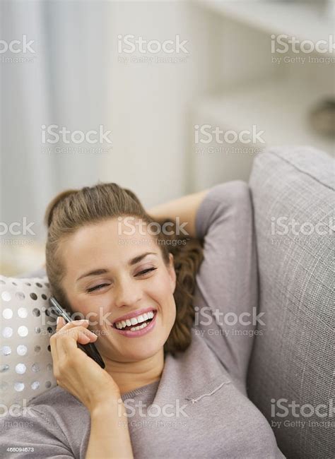 Happy Young Woman Talking Cell Phone While Laying On Sofa Stock Photo